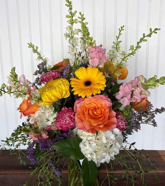 Bouquet of colorful flowers including yellow, orange, pink, and white flowers on a wooden surface.